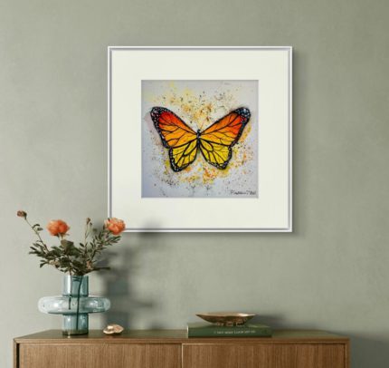Tablou Orange butterfly cu paspartu alb, pe un perete verde-gri, deasupra unei console cu flori