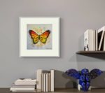 Acuarela Orange butterfly pe un perete gri, deasupra unor carti si a unui decor albastru