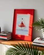 Tablou cu balerina in rochie rosie sprijinit de perete, pe un raft cu carti si frunze de palmier