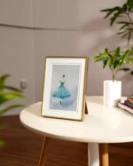 Tablou cu balerina in rochie turcoaz asezat pe o masa rotunda alba, langa o planta si carti